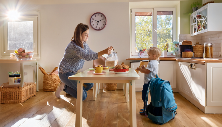 A sunlit family kitchen with a parent pulling an espresso shot while a child reaches for cereal across the table, school backpacks on the floor