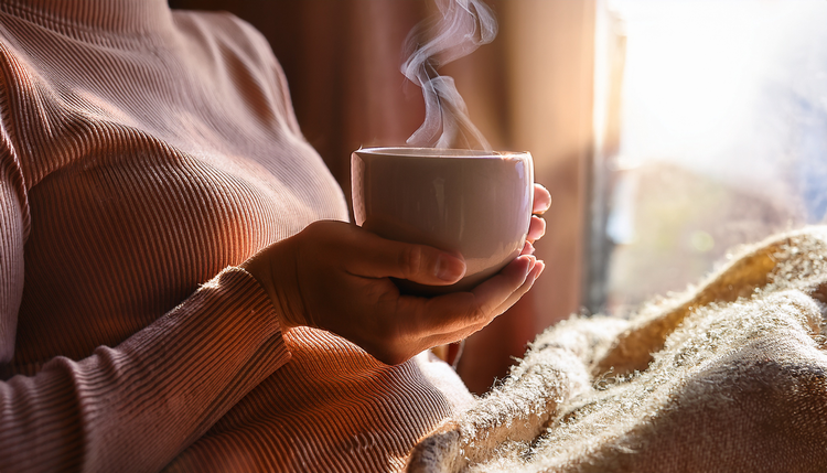Close-up of hands wrapped around a warm ceramic espresso cup at a windowsill, soft early morning light illuminating steam rising from the cup