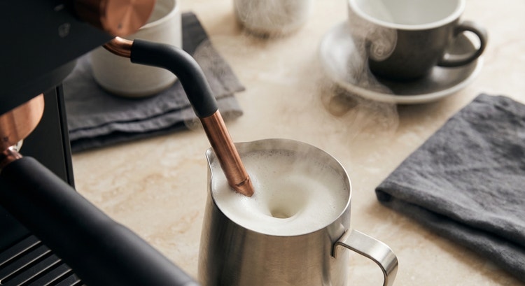 A barista pouring steamed milk into an espresso cup, creating a rosetta latte art pattern